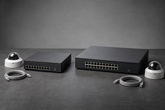 Two network video recorders of different sizes photographed side by side on a workbench, network cables and camera housings arranged around them
