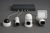 Switch with a row of different camera types connected to its ports, ranging from a compact dome to a large PTZ and a floodlight unit